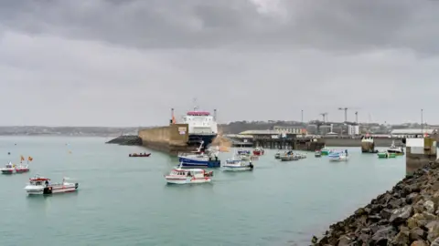 French fishing fleet is seen at the entrance to the harbour in St Helier, Jersey, A number of boats are in the water. 