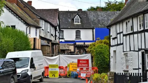 A road with a "road closed" sign and a residents access only - filming can be seen going on in the background. 