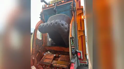 A sofa being loaded into a refuse vehicle.