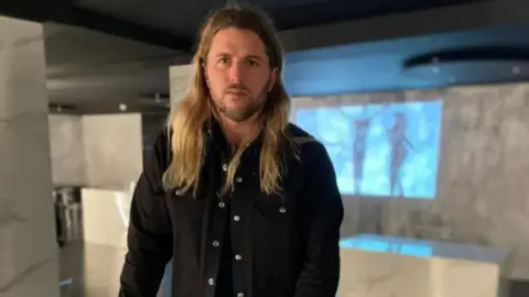 BBC celebrity chef Michael O'Hare in a dark shirt stands against a blurred background 