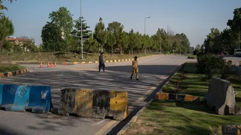 Getty Images Two people crossing a road which has been blocked off with concrete barriers