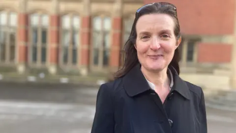 Dominque Moran from the University of Birmingham wears a black coat with a university building in the background