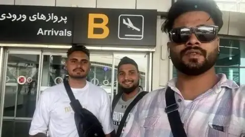 Three Indian men with sunglasses and shoulder bags standing in front of an airport in Tehran
