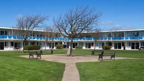 White and blue chalet accommodation at Pontins, Prestatyn, with a green square and benches