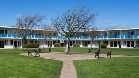 White and blue chalet accommodation at Pontins, Prestatyn, with a green square and benches