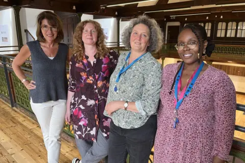 Kathryn Dixon, Cristina Carrasco, Barbara Basini and Chanel Nelson standing on the wooden floor of the Sunday School balcony