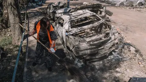 A woman sweeps the streets after damage from a Russian air strike in a residential area of Kyiv, Ukraine on 4July 2025.