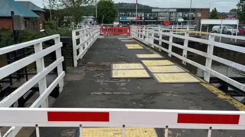 Image of Hempsted Bridge, with safety mats over the bumps in the tarmac. Red barriers block either side of the bridge. 