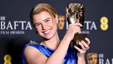 Getty Images Buckley has blonde hair which is tied back, she is holding up her BAFTA award and is wearing a blue dress.