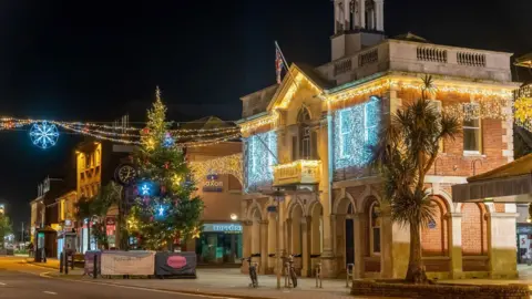 Christchurch town hall and high street at night adorned with Christmas lights and an illuminated Christmas tree