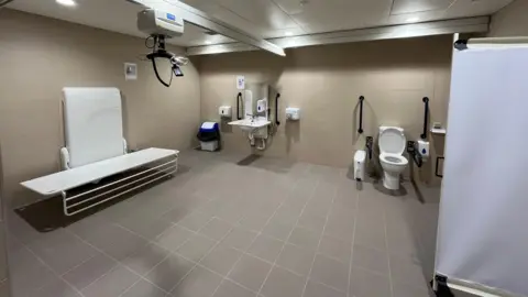 Four Seasons Mansfield accessible toilet, with a hoist, privacy curtain and disabled toilet and sink.