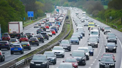 All three lanes on both sides of a motorway is packed with cars. A blue motorway safety sign is next to the left carriageway.
