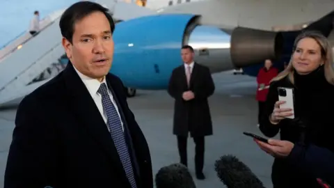 Mark Rubio in black coat with suit and tie talks to reporters