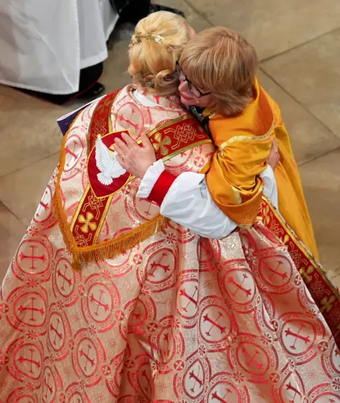 Gareth Fuller / PA Media Mullally embraces the Rt Rev Paulina Hlawiczka-Trotman, Bishop of the Lutheram Church of Great Britain, with her robe detail on display, during proceedings.