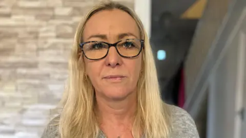 A blonde haired woman wearing black rimmed glasses looking at the camera 