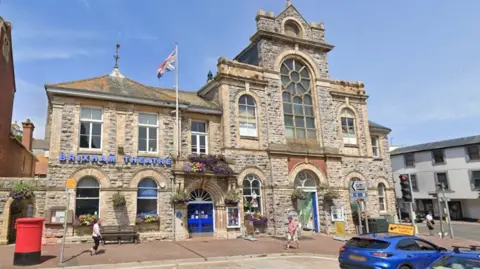 A two-storey granite public building with arched windows and doors and blue plastic letters saying Brixham Theatre.