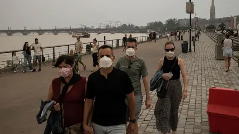 Getty Images People walking around with face masks on in Bordeaux, along a riverside cloaked in deep grey smoke