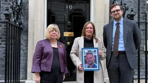 The three petitioners pose for a picture at the door of No 10. Jayne holds a framed picture of her son.