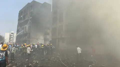 Rescue team members work as smoke rise at the crash site where an Air India plane crashed in Ahmedabad, India
