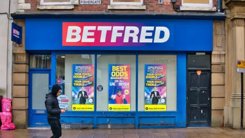 A branch of the Betfred bookmaker chain in a high street location on Fishergate in Preston in Lancashire in the north of the UK. A young person walks past as the rain falls. - stock photo
