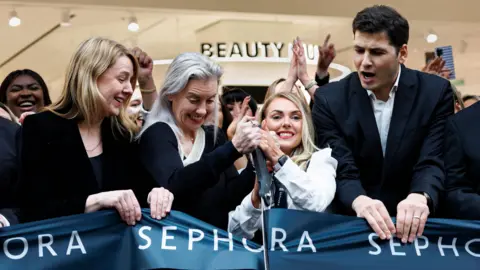 PA Media Three woman and a man holding the black Sephora ribbon as it is cut with a large pair of scissors.