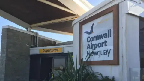 BBC Cornwall Airport Newquay's entrance with sign reading the name of the airport and a yellow rectangle sign reading departures.
