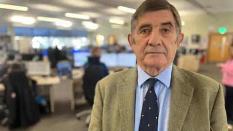 Police Commissioner Philip Wilkinson in the Wiltshire control room and call centre in Devizes. He is wearing a fawn-coloured jacket, a pale blue shirt and a dark tie with yellow spots on it