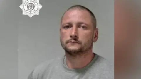 West Mercia Police A police mugshot of a man with a grey jumper. He has short dark hair and a short dark beard.