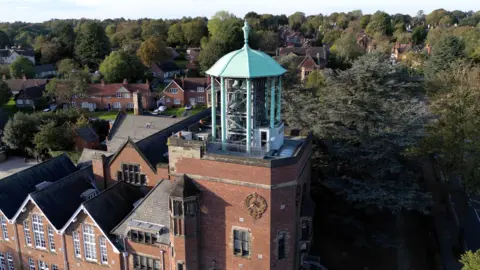 Bournville Village Trust An aerial view of a brown brick building with a central clock tower which has a blue metal structure on top with a bell inside