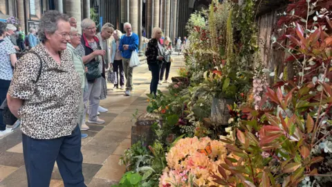A lady looking on at a flower display to the right. The display is in an array of colours inside the cathedral.