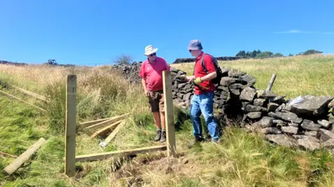 Photograph of volunteers installing leaky dams on Holcombe Moor. The image shows two people creating a wooden frame inside a gulley on the hillside.