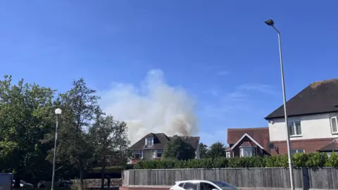A view of smoke coming from behind a house in an urban street. 