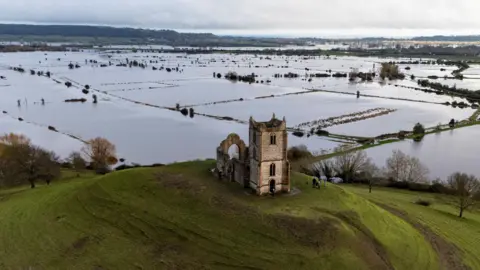 PA Media An old church on top of a Burrow Mump hill, with flooded fields behind