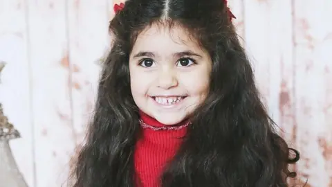 Family photograph Alice da Silva Aguiar, wearing a red jumper, smiles at the camera