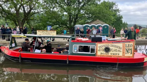A canal boat with a group of musicians performing for the crowd in the background.