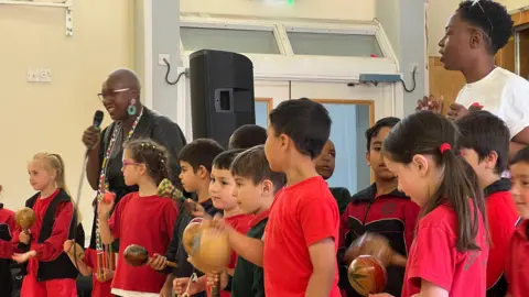 Pupils shake African instruments as members of the charity sing and dance 