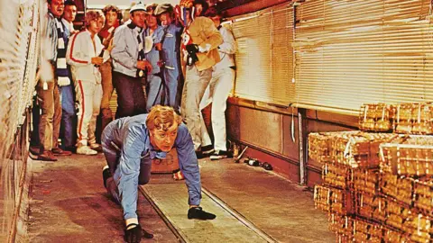 Silver Screen Collection/Getty Images Michael Caine, British actor, wearing blue overalls and crouching down with a stack of gold bullion in a publicity still issued for the film, 'The Italian Job', 1969.