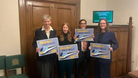 Helena Dollimore MP Four people holding signs with trains on them.