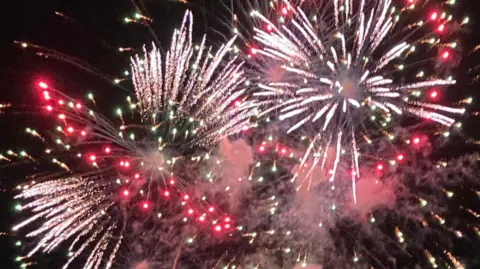 Large fireworks of white, red, pink and yellow going off in the nights sky.