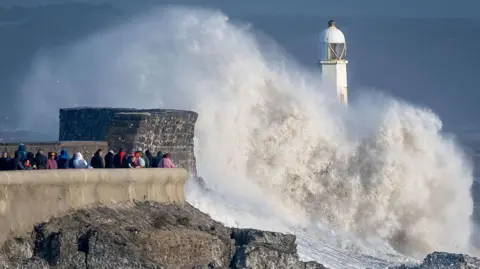 Getty Images Waves crash against the harbour wall in October last year in Porthcawl. Around 19 people are standing behind a lower wall watching.