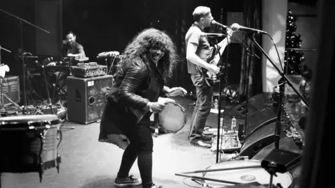 Denise Johnson on stage with a tambourine performing in a black and white photograph