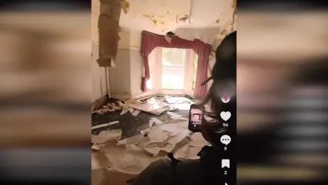 TikTok A person with a cap holds up a phone to capture the collapsed roof of an abandoned 