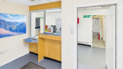 Shepherd Chartered Surveyors A reception desk with ceiling to desk screen is on the left. On the right is an open door leading into the reception area.