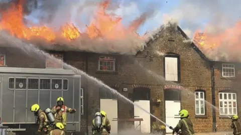Hook Norton Brewery stables ablaze with firefighters attempting to put it out with their hoses.