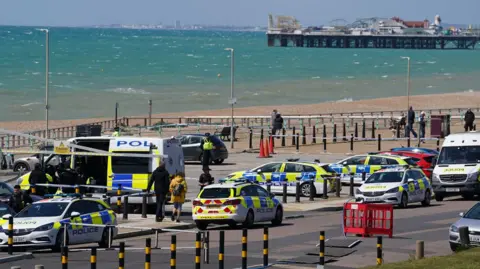 Various police vehicles in a car park on Brighton seafront. Brighton Palace Pier and a choppy sea are in the background