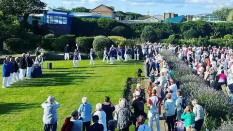 A bowling competition takes place at the Skegness bowling greens on North Parade. A large crowd watches the players walk on to the green. A large lavender border, with purple flowers, is also visible.