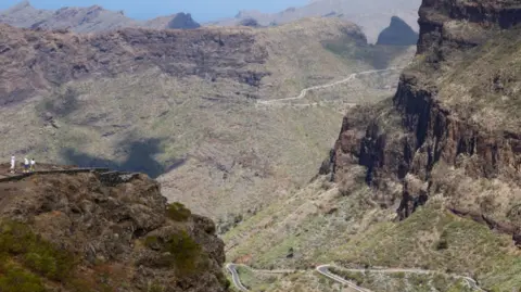 Reuters A view of a large cliff face looking down on to a winding road below in the Masca area of northern Tenerife. The land is dotted with cacti and the terrain is rough and hilly. 