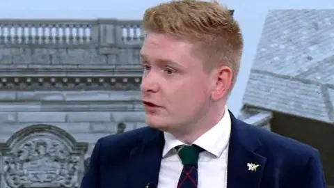 Richard Kilpatrick, wearing a white shirt, blue jacket and a tartan tie