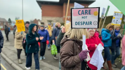 BBC Campaigners holding placards and marching through the streets of Belper. Placards read "Care not despair" and "Save our Ada"