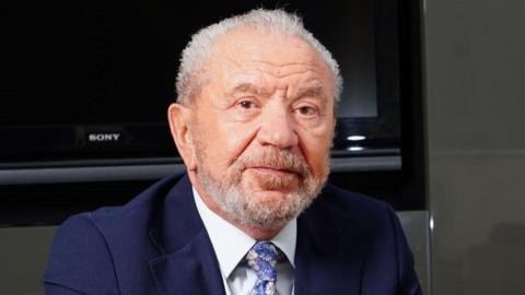 Lord Sugar wearing a white shirt and flowery tie and blazer